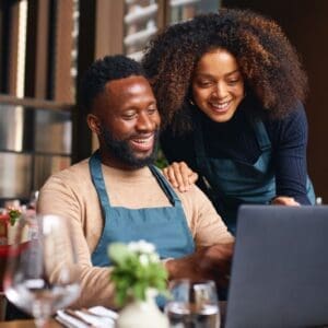 Black couple sitting at a table in a restaurant viewing a computer.